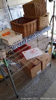 Full view of metal wire rack with wicker baskets on top, first aid box, and stacked boxes below containing books.