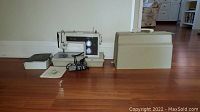 Electric sewing machine with foot pedal and beige carrying case on wooden floor
