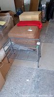 Full view of the metal shoe rack in a basement setting, showing all three shelves and legs.