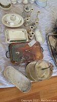 Wide view of silver plate trays and candle holders arranged on a surface showing tarnish and use.