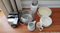 Photo showing Sunbeam toaster, stainless steel soup pot with glass lid, white thermos, ceramic jug, ceramic mug, and white bowl on floor.