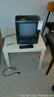 Citizen 10 inch CRT TV with VHS player and remote sitting on a light-colored wooden table, shown from left side angle.