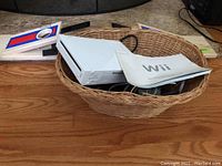 Nintendo Wii console inside wicker basket along with power cords and the Wii Operations Manual on top.