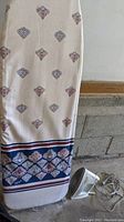 Full view of ironing board with patterned cover and Sunbeam iron placed on the floor next to it
