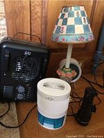 Photo showing SAI floor heater, Lonove white heater, ceramic lamp with floral shade, and black Garrity flashlight on wooden surface