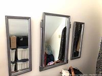 Three rectangular mirrors with grey wooden frames of varying sizes leaning against the wall indoors. Shows condition of frames and reflective surfaces.