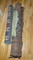 Three rolled and partially unrolled small rugs displayed on hardwood floor showing wear and tassel damage