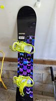 Full view of Burton Feel Good snowboard with attached yellow bindings showing color and design.