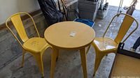 Photo showing yellow metal round bistro table with two matching chairs in a garage setting.