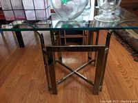 Photo showing glass top from side angle with chrome legs visible on hardwood floor.