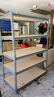 Full view of metal frame utility shelving unit with five particle board shelves, showing overall size and configuration in a garage setting.