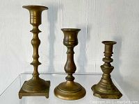 Three bronze candle holders placed side-by-side showing different heights and designs