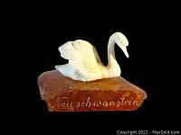 White carved swan figure on polished irregular amber base with 'Neuschwanstein' inscription on front.