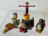 Front and side view of four antique character toys on clear acrylic stand with white background