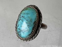 Close-up of large oval turquoise cabochon set in serrated bezel with twisted rope silver border on polished sterling silver band.