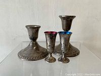 Four weighted sterling silver candlesticks: two large with wide ornate bases and two smaller with colored interiors (purple and blue).