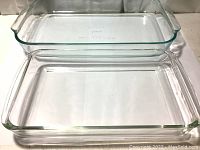 Top-down view of two clear glass rectangular Pyrex casserole dishes stacked, larger dish marked 234 with handles and smaller dish marked 232.
