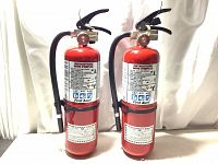 Two red fire extinguishers side by side showing full front label and black hose