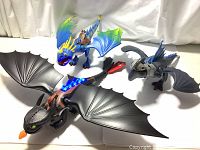 Three How to Train Your Dragon Playmobil dragons displayed: Toothless with light-up back fins, blue Stormfly with rider, and grey Drago figure.