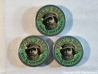 Three round sealed tins of Burt's Bees Res-Q Ointment arranged on a flat surface, showing all lids.
