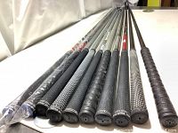 View of golf club grips showing a variety of black, perforated and textured styles primarily by Golf Pride, some wrapped in plastic.