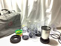 Full lot view showing Magic Bullet branded carry bag, mixer base, multiple blending cups, colored measuring rings, and lids.
