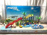 Front view of the Playmobil Summer Fun diorama featuring the water park with red slide, pools, and multiple mini-figures arranged engaging in summer activities
