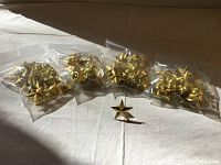 Five clear plastic bags containing gold star pin badges arranged in a row with one loose pin badge in front.