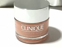 Front view of Clinique Moisture Surge 72H Auto-Replenishing Hydrator in a frosted peach glass jar with silver lid showing brand and product name.