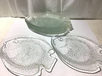View of all eight clear glass fish-shaped plates stacked and spread out to show shape and texture.