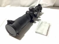 Black matte illuminated crossbow scope with front and rear flip-up lens caps closed, displayed with premium cleaning cloth.