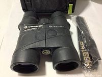 Top view of black Vanguard Orros 8x42 binoculars with included neck strap beside them, showing the labeling and rubberized exterior.