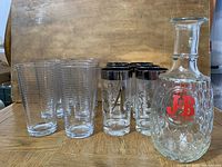 Photo of six HB glasses with silver rings, six ribbed clear glasses, and J&B Rare Scotch decanter on wooden surface