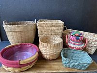 Photo showing seven woven baskets including the Longaberger basket with plastic chip and dip insert, small greenish-blue basket, basket with pink rim and plastic insert, and the colorful lidded basket