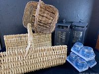 Photo shows one curly willow basket with handle, one log carrier basket, two black metal lanterns with glass panels, and three sets of tealight jars in plastic holders.