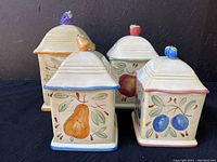 Four square ceramic canisters with lids featuring fruit motifs and sculpted fruit handles. Varied sizes 8-12 inches.