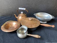 Photo showing the copper tea kettle with porcelain and copper handle, copper pan with wooden handle and lid, Preismer pewter saucepan with wooden handle, and large copper bowl with handles.