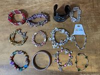 All twelve bracelets arranged on a wooden surface showing variety of styles including cuff, bangle with rhinestones, beaded stretch and charm bracelets.