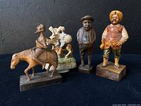 Photo showing four figurines including porcelain music box and three carved wooden figurines against black background