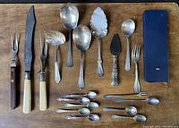 Full layout of all flatware pieces and serving utensils including spoons, forks, pie server, cheese server, and zipper case with additional items.