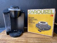Photo of Keurig B40 coffee maker and Kodak Carousel 750H projector box side-by-side on wooden surface