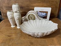 Photo showing a Lenox mantel clock, three white ceramic vases with rose motifs, a large shell-shaped serving dish, and an Orchard In Bloom Peach dip bowl in its box, all arranged on a wooden surface.