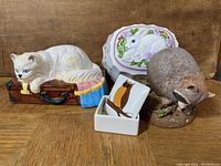 Lot overview with four items displayed: musical cat figurine on suitcase, bunny-themed trinket dish, raccoon figurine, and bunny cake mold.