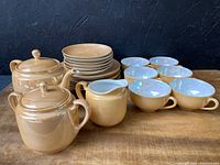 Full set displayed on wooden table showing tea pot, sugar bowl, creamer, cups and plates with warm orange lusterware finish.