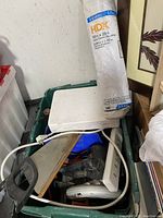 Photo showing a green bin containing a Black & Decker electric jigsaw, power strip, and clear plastic sheeting roll.