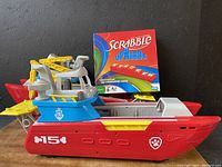 Photo showing one Paw Patrol amphibious toy boat and Scrabble Upwords Stackem game box in background
