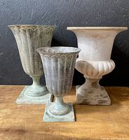 Photo showing two green patina brass urns with scalloped edging and one white ceramic urn with classical shape.