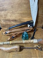Photo showing vintage glass insulator with crack, black metal wrench, four wooden weaving shuttle holders, primitive broom, and leather sword holder with canvas strap.