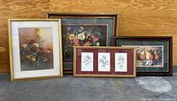 Four framed wall art prints including floral and fruit themes arranged on the floor, showing size and framing