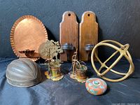 Wide shot showing all items: copper wall sconce, wooden sconces, metal helmet mold, two small metal sculptures, metal armillary sphere, and round painted shaving soap box.